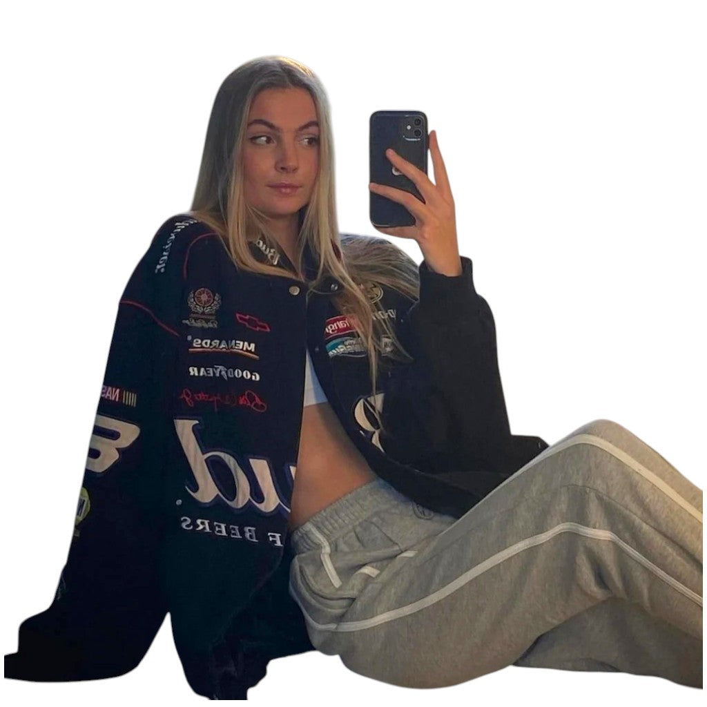 Person wearing a navy jacket with various logos, sitting and taking a selfie.