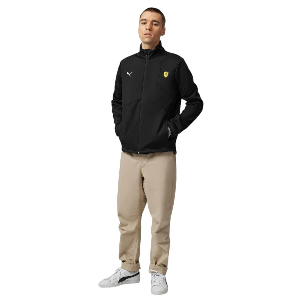 Person wearing a black jacket with a logo and beige pants on a white background
