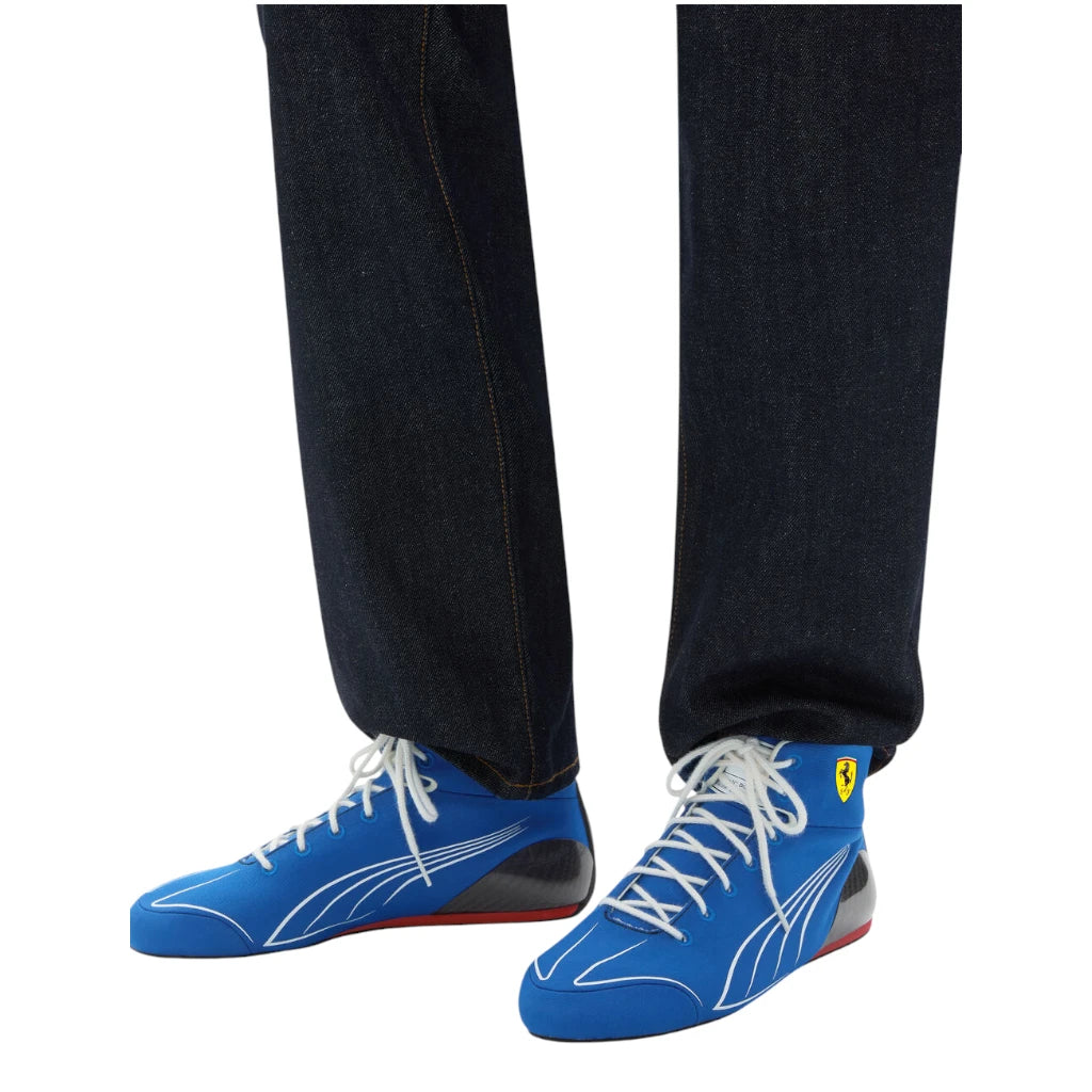 Blue high-top sneakers with white laces and a red sole worn with black pants on a white background.