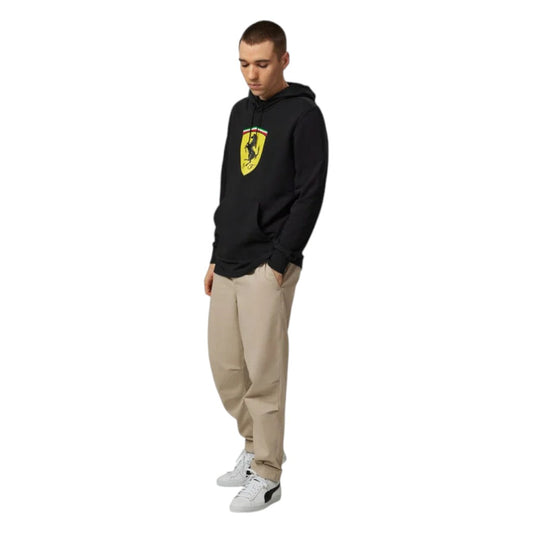 Person wearing a black hoodie with a logo and beige pants on a white background