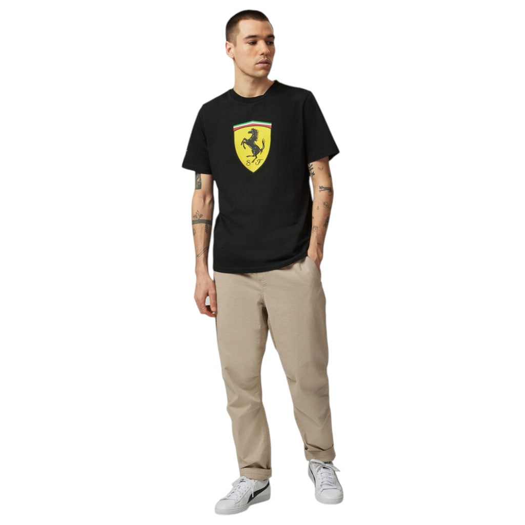Man wearing a black t-shirt with a logo and beige pants on a white background