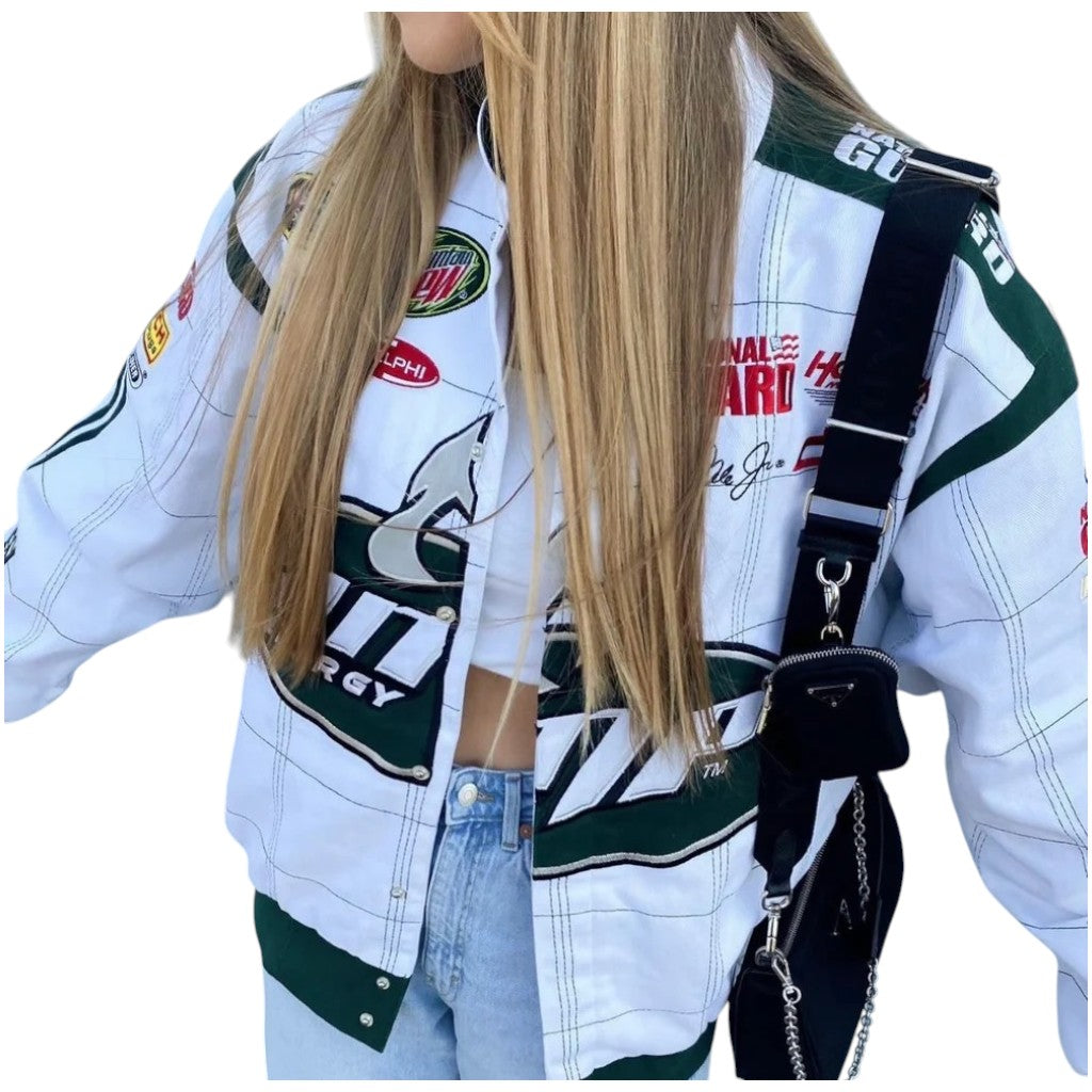 Person wearing a white racing jacket with various logos and a black bag over one shoulder.