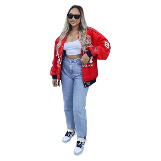 Woman wearing a red varsity jacket, white crop top, and blue jeans on a white background