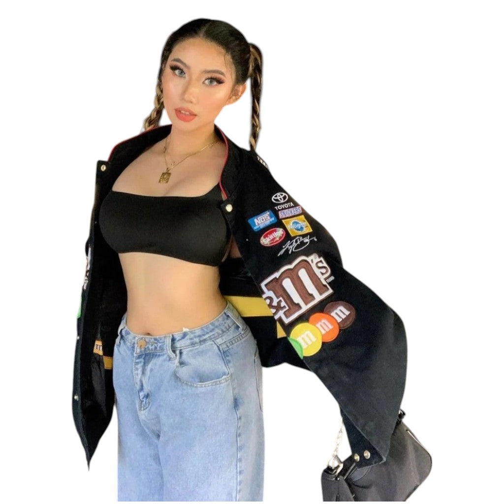 Person wearing a black varsity jacket with logos, black crop top, and blue jeans on a white background