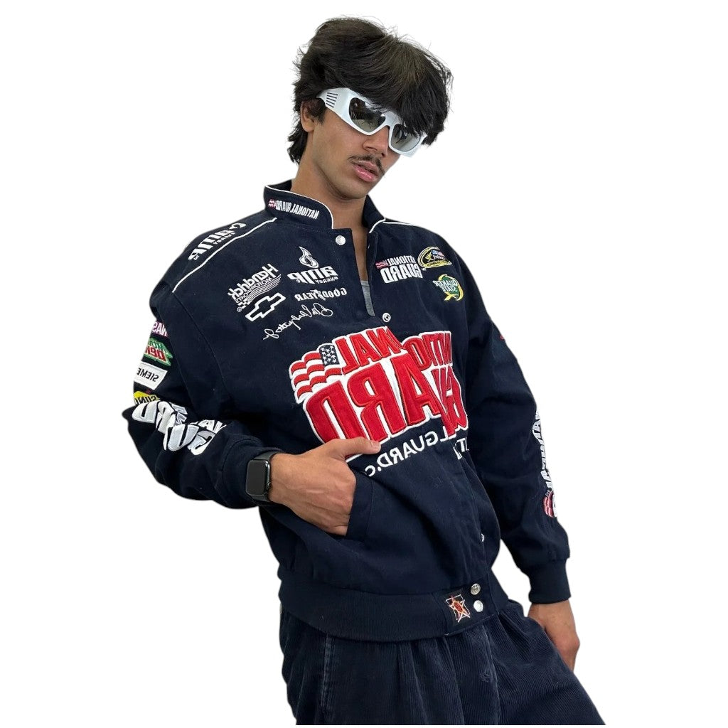 Person wearing a navy blue racing jacket with various logos on a white background
