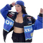 Woman wearing a blue racing jacket with various sponsor logos on a white background
