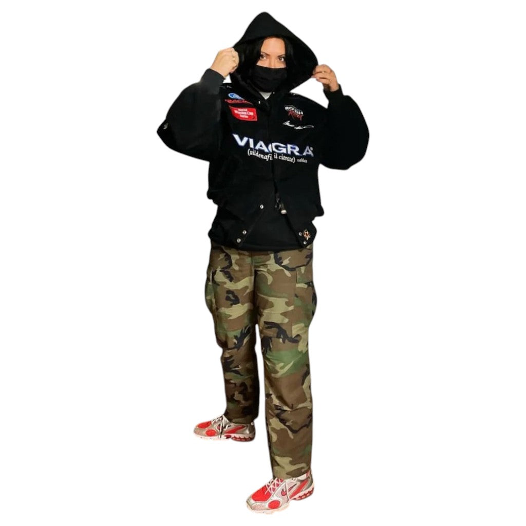 Person wearing a black hoodie with visible branding and camouflage pants on a white background